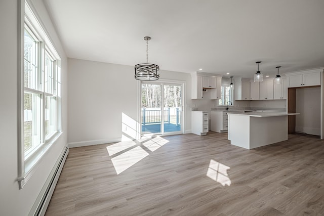 kitchen featuring decorative light fixtures, white cabinets, a center island, and baseboard heating