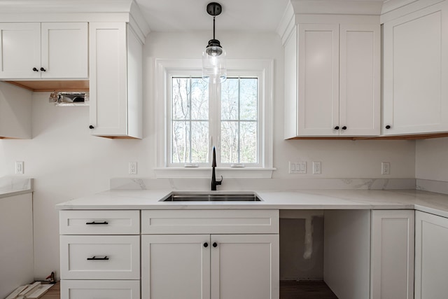 kitchen with sink, light stone counters, hanging light fixtures, and white cabinetry