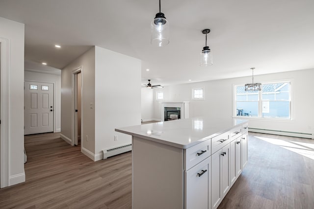 kitchen with hanging light fixtures, a kitchen island, a baseboard heating unit, light wood-type flooring, and white cabinetry