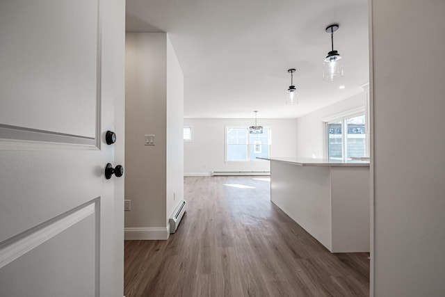 corridor with wood-type flooring, baseboard heating, and a notable chandelier