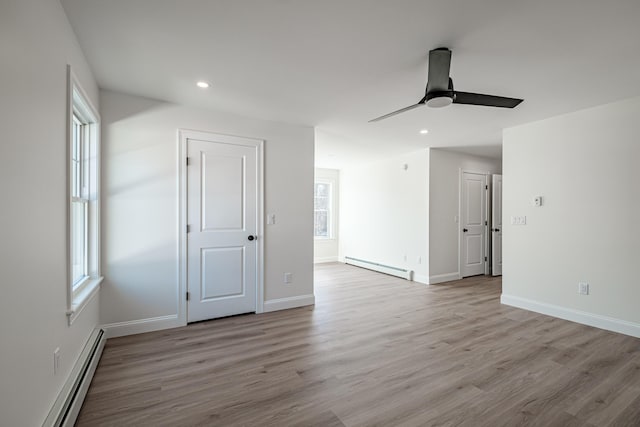 empty room featuring a baseboard heating unit, light wood-type flooring, ceiling fan, and plenty of natural light