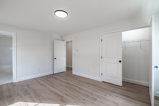 unfurnished bedroom with ensuite bath, a closet, and light wood-type flooring