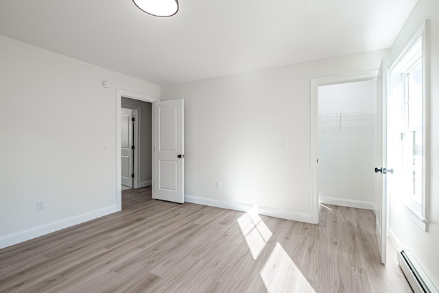 unfurnished bedroom featuring a closet, a walk in closet, a baseboard heating unit, and light hardwood / wood-style flooring