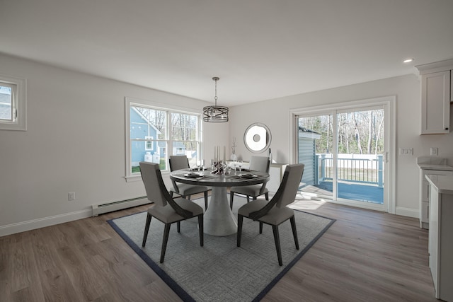 dining room featuring a notable chandelier, baseboard heating, hardwood / wood-style flooring, and plenty of natural light