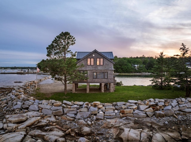 back house at dusk featuring a lawn and a water view