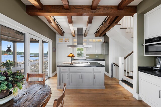 kitchen with stainless steel oven, track lighting, island exhaust hood, white cabinetry, and a water view