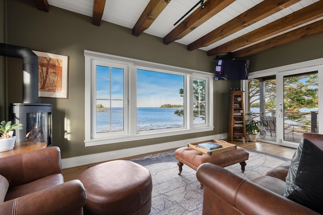 living room featuring plenty of natural light, light wood-type flooring, a wood stove, and beamed ceiling