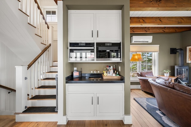 bar featuring beam ceiling, a wall mounted AC, light hardwood / wood-style floors, and stainless steel oven