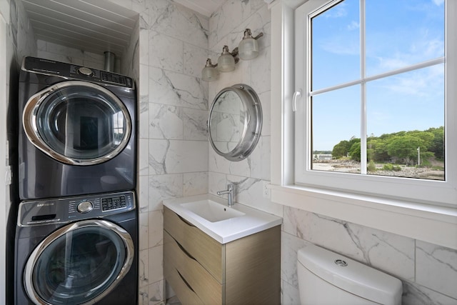 clothes washing area featuring tile walls, sink, and stacked washer and dryer