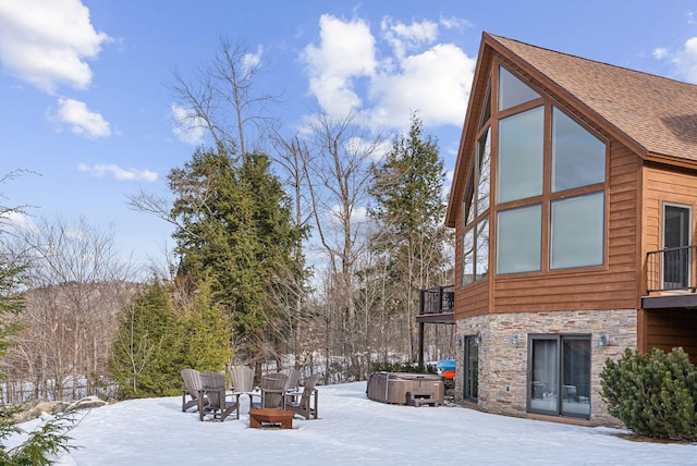 snowy yard featuring a balcony, a hot tub, and a fire pit