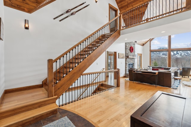 staircase featuring wood ceiling, hardwood / wood-style flooring, a stone fireplace, and high vaulted ceiling