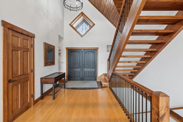 foyer entrance with light wood-type flooring, a chandelier, and a towering ceiling