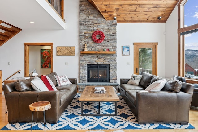 living room featuring high vaulted ceiling, light hardwood / wood-style flooring, a stone fireplace, and wooden ceiling