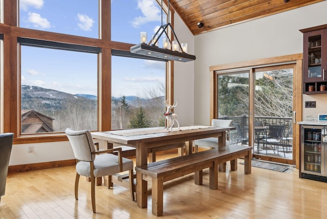 dining room featuring beverage cooler, light wood-type flooring, wood ceiling, vaulted ceiling, and a mountain view