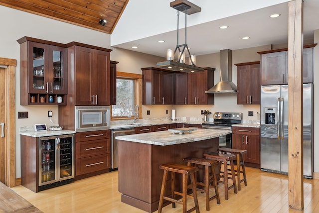 kitchen with beverage cooler, a center island, wall chimney range hood, stainless steel appliances, and hanging light fixtures