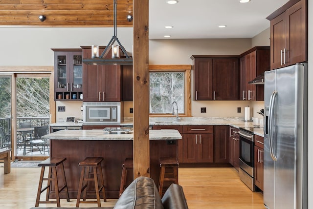 kitchen featuring pendant lighting, sink, appliances with stainless steel finishes, a kitchen breakfast bar, and light stone counters