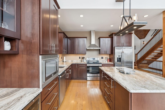 kitchen with light hardwood / wood-style floors, appliances with stainless steel finishes, light stone countertops, pendant lighting, and wall chimney range hood