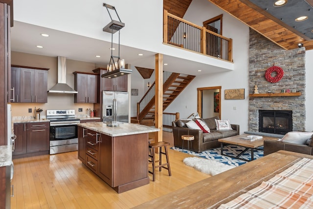 kitchen featuring stainless steel appliances, a fireplace, light stone countertops, a kitchen island, and wall chimney exhaust hood