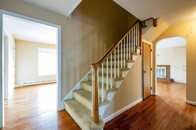 stairway featuring wood-type flooring, a baseboard heating unit, and a fireplace