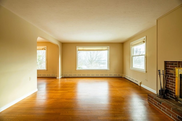 unfurnished living room featuring a wealth of natural light, a fireplace, baseboard heating, and hardwood / wood-style flooring