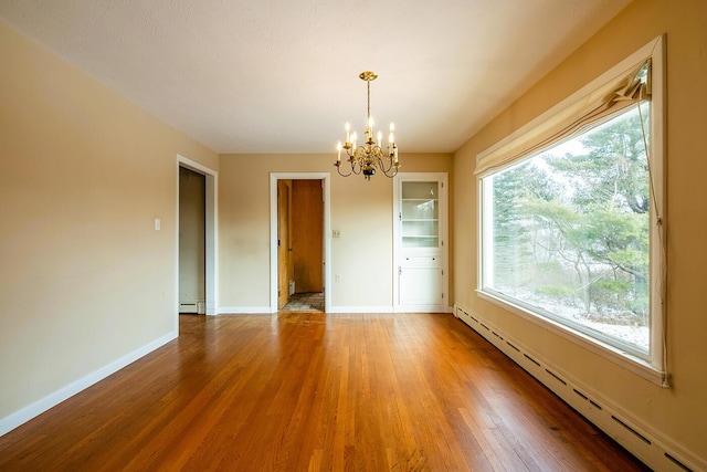 spare room featuring a baseboard heating unit, an inviting chandelier, and hardwood / wood-style flooring