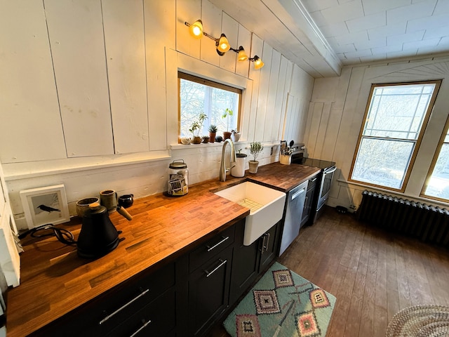 kitchen featuring appliances with stainless steel finishes, radiator, butcher block countertops, white cabinets, and sink