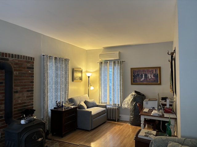 living room with radiator, a wall mounted AC, a wood stove, and light hardwood / wood-style flooring