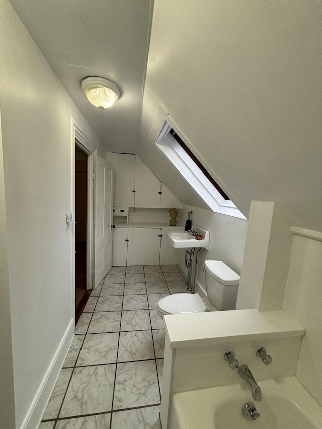 bathroom featuring vaulted ceiling with skylight, toilet, and a bathing tub