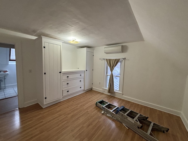 unfurnished bedroom with hardwood / wood-style floors, a wall unit AC, and a textured ceiling