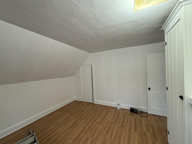 additional living space featuring hardwood / wood-style flooring, a textured ceiling, and vaulted ceiling