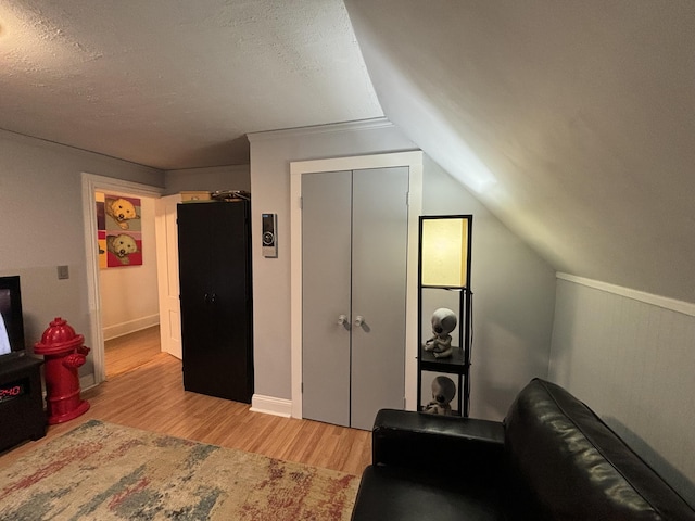 bedroom with light hardwood / wood-style floors, a textured ceiling, a closet, and lofted ceiling