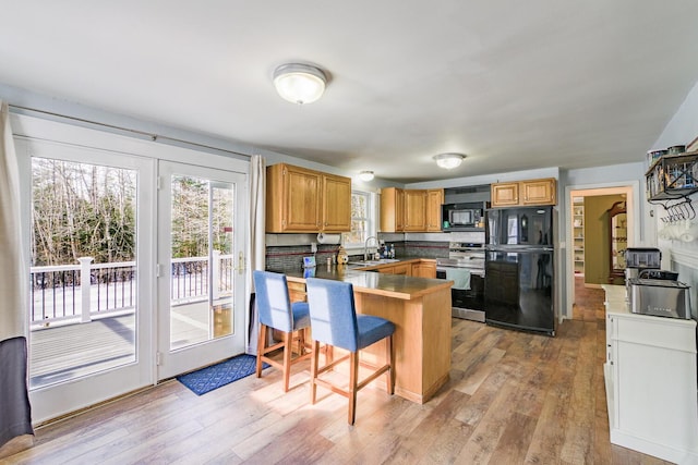 kitchen with black appliances, a breakfast bar, kitchen peninsula, sink, and light hardwood / wood-style flooring