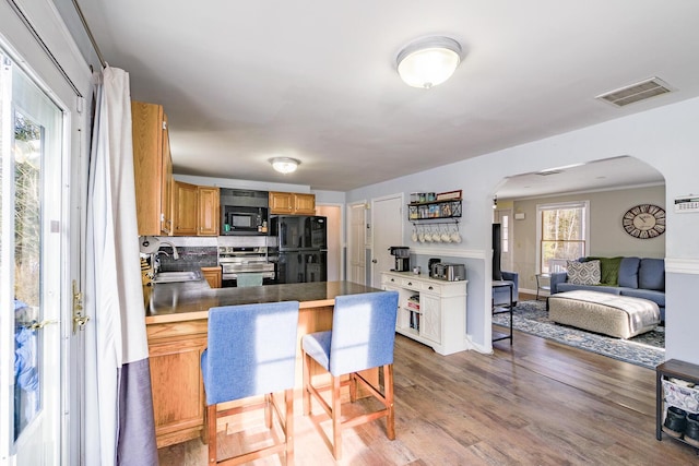 kitchen with a kitchen bar, kitchen peninsula, dark wood-type flooring, black appliances, and sink