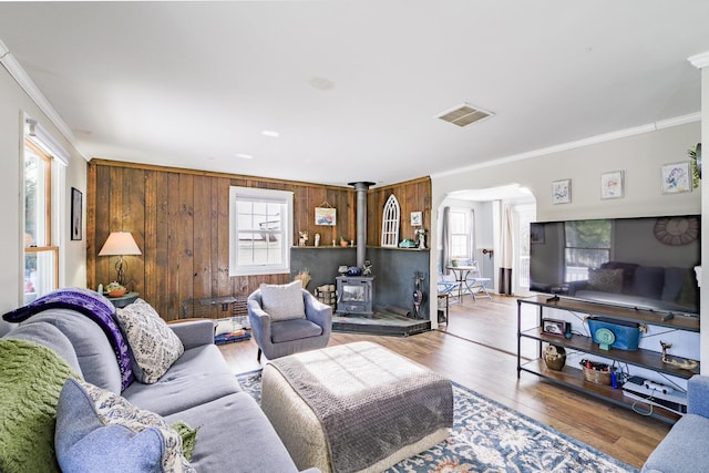 living room featuring crown molding, wooden walls, a wood stove, and hardwood / wood-style floors