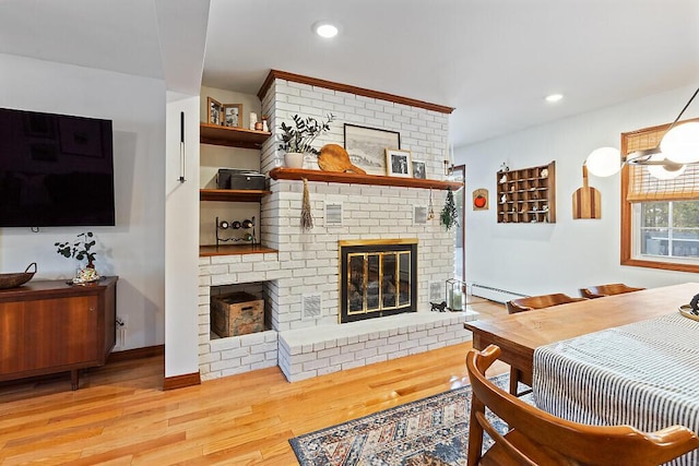 living room featuring a brick fireplace, a baseboard radiator, and light hardwood / wood-style floors