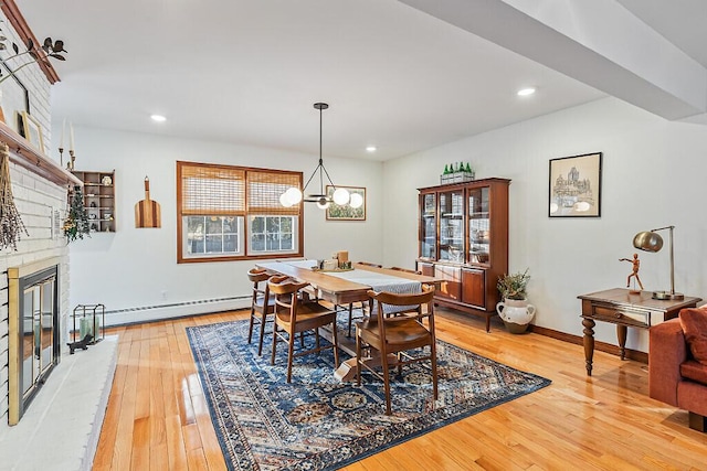 dining space featuring a notable chandelier, wood-type flooring, a fireplace, and a baseboard heating unit