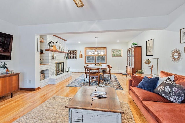 living room with ceiling fan with notable chandelier, a brick fireplace, light hardwood / wood-style floors, and baseboard heating