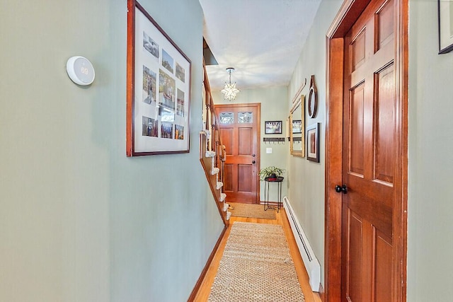 hall with light wood-type flooring, a baseboard radiator, and an inviting chandelier