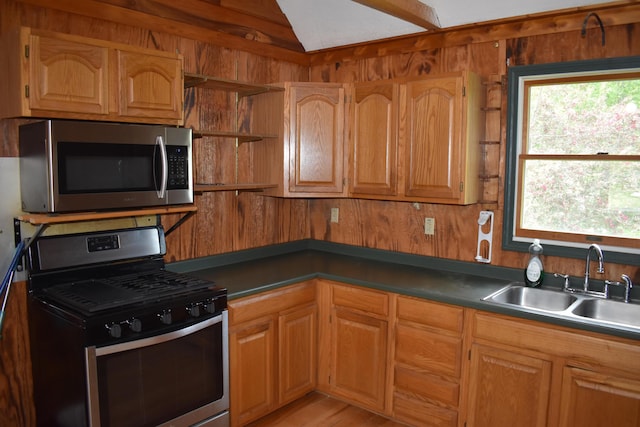 kitchen with light wood-type flooring, stainless steel appliances, wooden walls, and sink