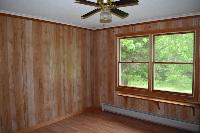 unfurnished room with hardwood / wood-style flooring, wood walls, ceiling fan, a baseboard radiator, and crown molding