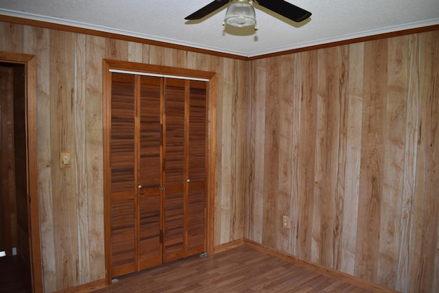 unfurnished bedroom featuring wood walls, ceiling fan, a closet, wood-type flooring, and ornamental molding