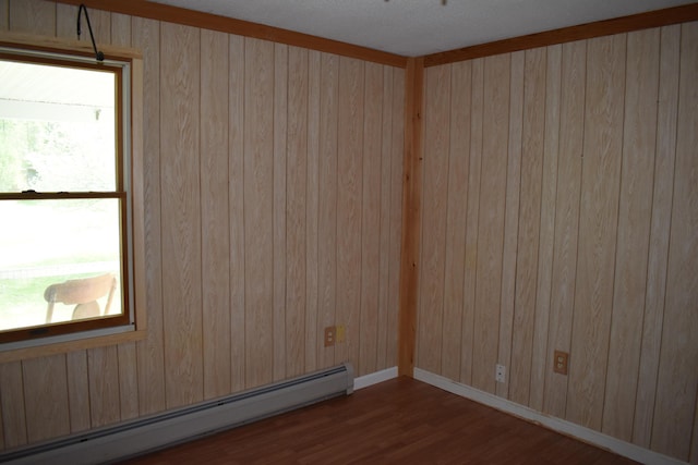 unfurnished room featuring a baseboard heating unit, wood walls, and wood-type flooring