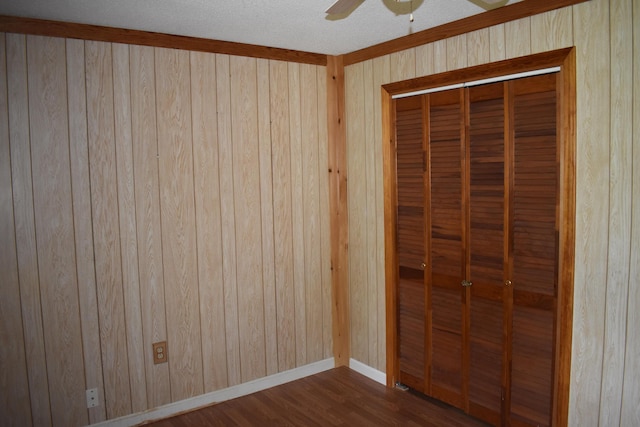 unfurnished bedroom with dark wood-type flooring, a closet, wooden walls, and ceiling fan