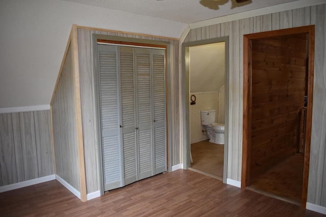 unfurnished bedroom featuring lofted ceiling, wood-type flooring, a closet, wood walls, and ceiling fan