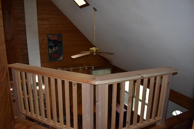 stairway featuring ceiling fan, vaulted ceiling with skylight, and wood walls