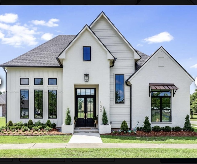 modern farmhouse style home featuring roof with shingles, french doors, board and batten siding, and a front yard