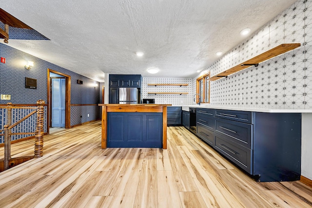 kitchen with sink, blue cabinets, light wood-type flooring, wood counters, and stainless steel refrigerator