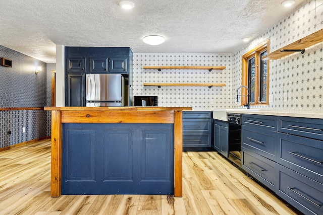 kitchen with light hardwood / wood-style floors, stainless steel fridge, blue cabinetry, and a textured ceiling