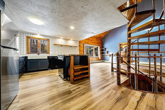 interior space with sink, wooden walls, vaulted ceiling, black dishwasher, and stainless steel fridge