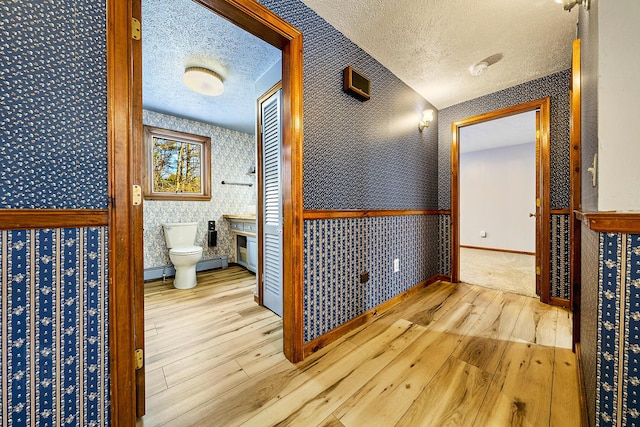 hall featuring a baseboard heating unit, a textured ceiling, and light hardwood / wood-style flooring